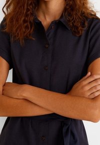 Chemise bleu marine à manches courtes avec col, dotée d'une ceinture ajustée à la taille et de boutons en bois, fabriquée dans un tissu léger.