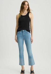 Top a costine nero con scollatura rotonda, abbinato a jeans svasati blu chiaro con dettagli decorativi all'orlo. Sandali neri con tacco.