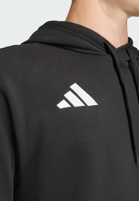 Hoodie noir en tissu doux, arborant un logo Adidas blanc avec trois bandes diagonales sur la poitrine supérieure gauche et une capuche avec cordon de serrage.