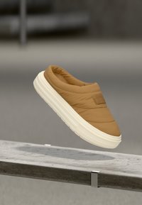 Ταμπά, καπιτονέ παπούτσι τύπου slip-on με στρογγυλεμένη μύτη και παχιά λευκή σόλα. Διαθέτει υφασμάτινη επιφάνεια και διακριτική ετικέτα με το λογότυπο στην επάνω πλευρά.