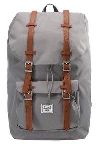 Sac à dos gris avec des sangles en cuir marron, boucles argentées, poche avant, fermeture à cordon et un patch logo Herschel blanc sur la poche avant.