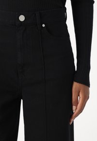 Zwarte denim high-waisted jeans met een gladde textuur, voorzien van een metalen knoopsluiting, voorzakken en details in de zijnaad.