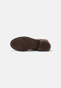 Semelle de chaussure en caoutchouc marron avec motif antidérapant texturé et profondeur modérée. Comprend une empreinte du logo de la marque et des détails d'accent hexagonaux.