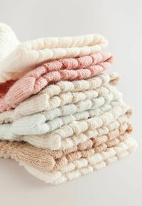 Pila di sei calze lavorate a maglia in crema, rosa pallido, verde chiaro e beige, che mostrano un design a coste testurizzato con risvolti.