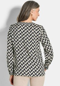 Haut à manches longues noir et crème avec un motif en chevrons, présentant des détails froncés aux manches et une coupe décontractée. Texture de tissu douce.