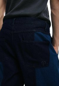 Traperice imaju dizajn patchwork u tamnoplavim i srednjoplavi tonovima. Stražnji džepovi imaju suptilan logo akcent. Teksturalna tkanina sa standardnim šavovima.