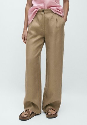 Pantalon large en lin marron clair avec une fermeture à bouton, des poches latérales et une texture lisse, associé à des sandales marron.