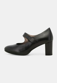 Scarpa nera in pelle con tacco alto, punta rotonda, dettaglio intagliato sulla tomaia e una larga cinghia sul piede. Design con tacco a blocco.