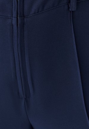 Granatowe spodnie dopasowane o gładkiej fakturze, z zamkiem błyskawicznym, kieszeniami z przodu i zakładkami dla uzyskania strukturalnego wyglądu.