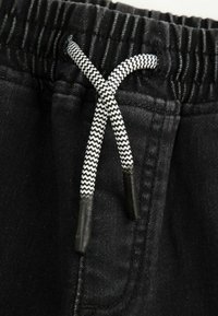 Czarne dresy mają elastyczny pasek w talii z białą i czarną sznurkiem w wzór zygzakowy. Zbliżenie na materiał i detale szwów.