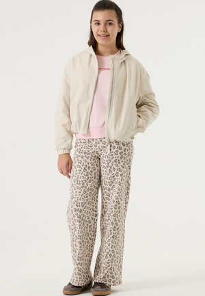 Light beige zip-up hooded jacket over a pink sweatshirt, paired with loose-fitting leopard print pants and brown shoes.