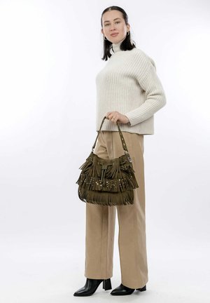Borsa a tracolla verde oliva con frange e accenti metallici, realizzata in morbido suede, con forma arrotondata e tracolla regolabile, abbinata a pantaloni beige.