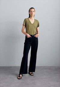 Olive green V-neck T-shirt with short sleeves, paired with high-waisted black wide-leg pants and black strappy sandals. Minimalist design.