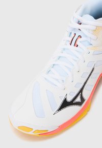 Buty sportowe w białej siateczce z czarnymi i pomarańczowymi akcentami. Posiadają kolorową podeszwę w żółtym i różowym kolorze, która wyróżnia się zaokrąglonym kształtem i teksturowanymi detalami.