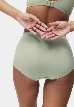 Lichtgroene, hooggesneden ondergoed met een gladde stof, naadloze randen en een aansluitend ontwerp. Handen dicht bij de tailleband geplaatst.