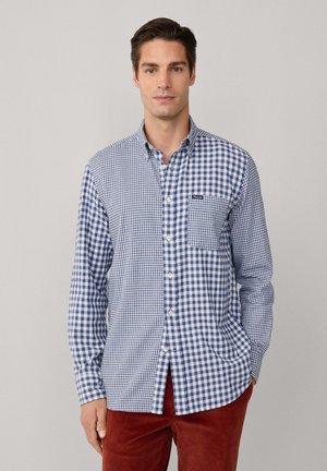 Blau-weißer karierten Button-Down-Hemd mit langen Ärmeln, einer einzelnen Brusttasche und kontrastierendem Stoffmuster. Getragen mit roten Cordhosen.