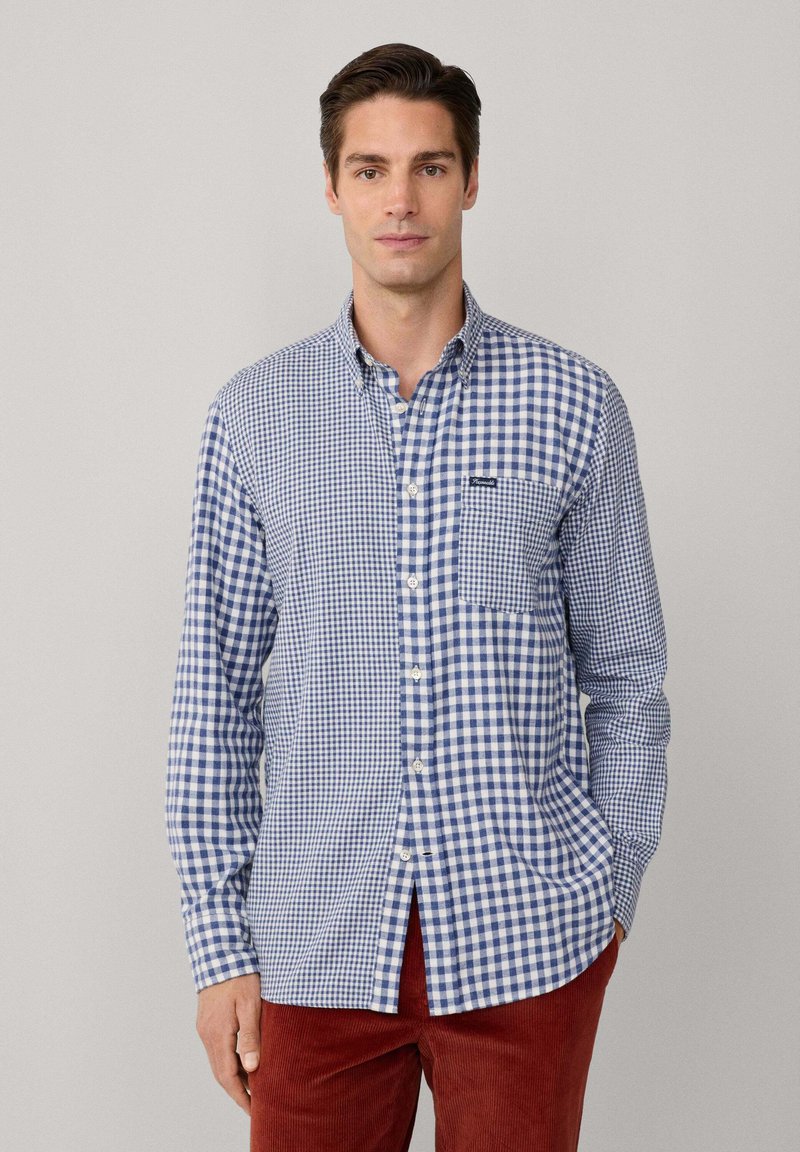 Blau-weißer karierten Button-Down-Hemd mit langen Ärmeln, einer einzelnen Brusttasche und kontrastierendem Stoffmuster. Getragen mit roten Cordhosen.