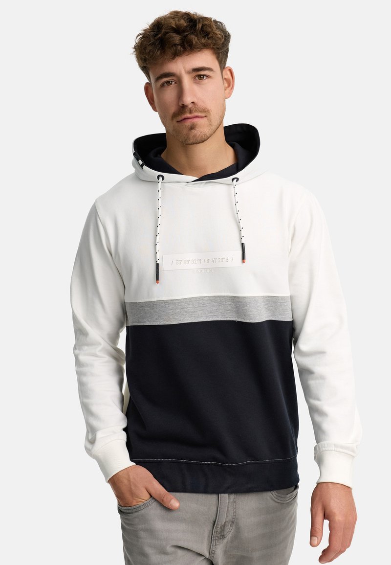 Hættebluse med en farveblokdesign i hvid, grå og marineblå, lavet af blødt stof med snore og et trykt mærke.