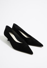 Zapatos de tacón en ante negro con punta afilada y tacón bajo. Presentan un forro interior suave y un sutil corte a lo largo del borde superior.