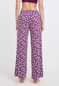 Paarse bloemenprint wijdlopende broek met een elastische tailleband, met een witte botanische print tegen de donkere achtergrond.