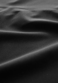 Material negru neted cu pliuri subtile și iluminare blândă care evidențiază textura și curburile delicate.