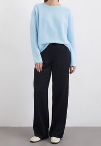Pull tricoté bleu clair à manches longues associé à un pantalon noir à jambes larges. La tenue est complétée par des chaussures blanches à enfiler.