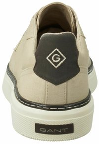 Beige Leinenschuhe mit schwarzem Gummi-Fersenelement und geprägt Logo. Mit einer weißen Sohle und kontrastierenden Nähdetails.