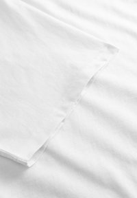 Nærbillede af en hvid T-shirt-ærme med synlige syninger på en glat stofbaggrund.