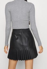 Pull gris côtelé à manches longues associé à une mini-jupe plissée en similicuir noir, présentant une texture lisse et une forme structurée.