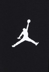 Un tissu noir arborant un logo Jumpman blanc en pleine action, affichant une pose dynamique avec un ballon de basket au-dessus de sa tête.