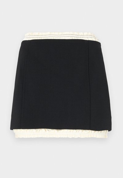 Juodas sijonas su banguotu dramblio kaulo kraštu, pasižymintis paprasta forma ir švariomis linijomis. Pagamintas iš lygaus audinio su nedideliu tekstūros efektu.