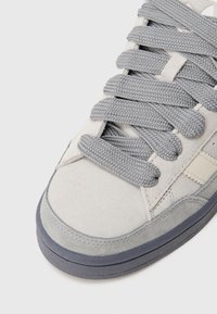 Světlé šedé tenisky z broušené kůže se silnými šedými tkaničkami, texturovanou stélkou a hladkou kontrastní tmavě šedou gumovou podrážkou.