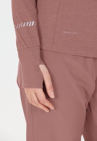 Close-up van een hand van een persoon naast hun heup, die een mauve lange mouwtop met duimopening en bijpassende mauve broek draagt.