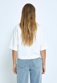 Camiseta blanca cortada con mangas cortas, combinada con unos vaqueros de tiro alto en azul claro. Tejido suave con un detalle mínimo.
