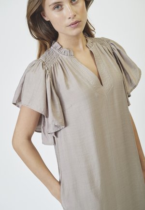 Robe beige claire avec des manches courtes à volants et un col en V. Texture lisse avec un subtil détail de plissage sur le corsage et des poches latérales.