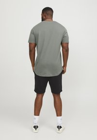 Light green cotton t-shirt with a rounded hem, paired with black shorts. Model wears white sneakers with black accents and striped socks.