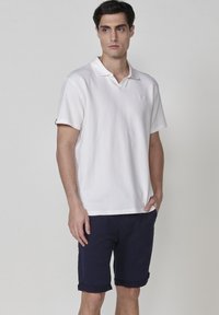 Vit, texturerad polo med krage och korta ärmar, i kombination med marinblå shorts med uppvikt fåll. Minimal logotyp synlig.