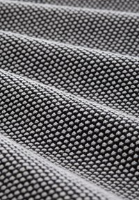 Texturerat tyg i svart och vitt, med ett mönster av små upphöjda prickar som är ordnade i rader. Ytan ser mjuk och följsam ut.