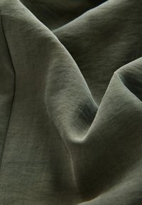 Olivově zelená tkanina s měkkou, hladkou strukturou, s jemnými vráskami a záhyby, které zvýrazňují její plynulý design.