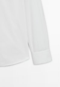 Hvid skjortebluse med lange ærmer, manchet og sidesømme, vist mod en ensfarvet hvid baggrund.