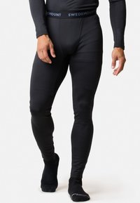 Zwarte thermoleggings van rekbaar materiaal, met een merkband in de taille. Strak, figuurvormend ontwerp met een gladde textuur.