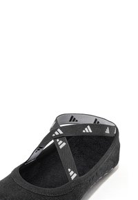 Black athletic shoe with cross straps, soft textile upper, textured interior, and white accent patterns on the straps and sole.