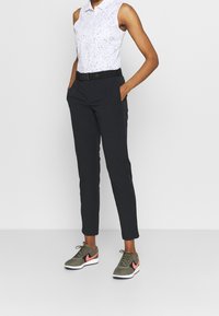 Ärmlös vit polo med svarta prickar, svart bälte och mörkgrå smalare byxor. Olibero gröna sneakers med rosa detaljer.