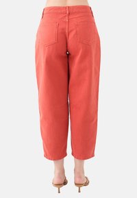 Jeans cropped di un arancione ruggine con vita alta, tasche posteriori e una vestibilità rilassata. Il tessuto presenta una texture liscia e resistente.