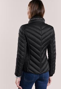 Giacca a vento nera con motivo a rombi, colletto alto e dettagli in cerniera argentati, abbinata a jeans blu.