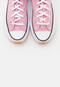 Pink canvas sneakers feature white laces, a white rubber toe cap, and a black trim along the sole, with a textured gum rubber outsole.