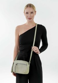 Borsa a tracolla in pelle verde chiaro con tasca frontale con zip e tracolla regolabile, caratterizzata da una texture morbida e curve fluide.