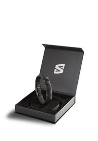 Schwarzes Armband in einer Präsentationsbox, mit strukturiertem Gewebe und glatten metallischen Akzenten. Die Box ist schwarz mit einem weichen Innenraum.