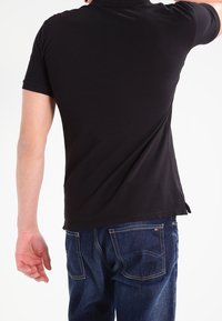 Svart kortärmad polo med krage, med rak fåll och sidesprund, parat med mörkblå denimjeans.