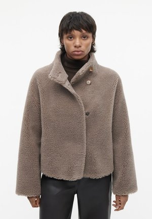 Geknipte, bruine fleece jas met een sjawlnek, twee bruine knopen en brede mouwen. Textuurstof voor warmte en comfort.